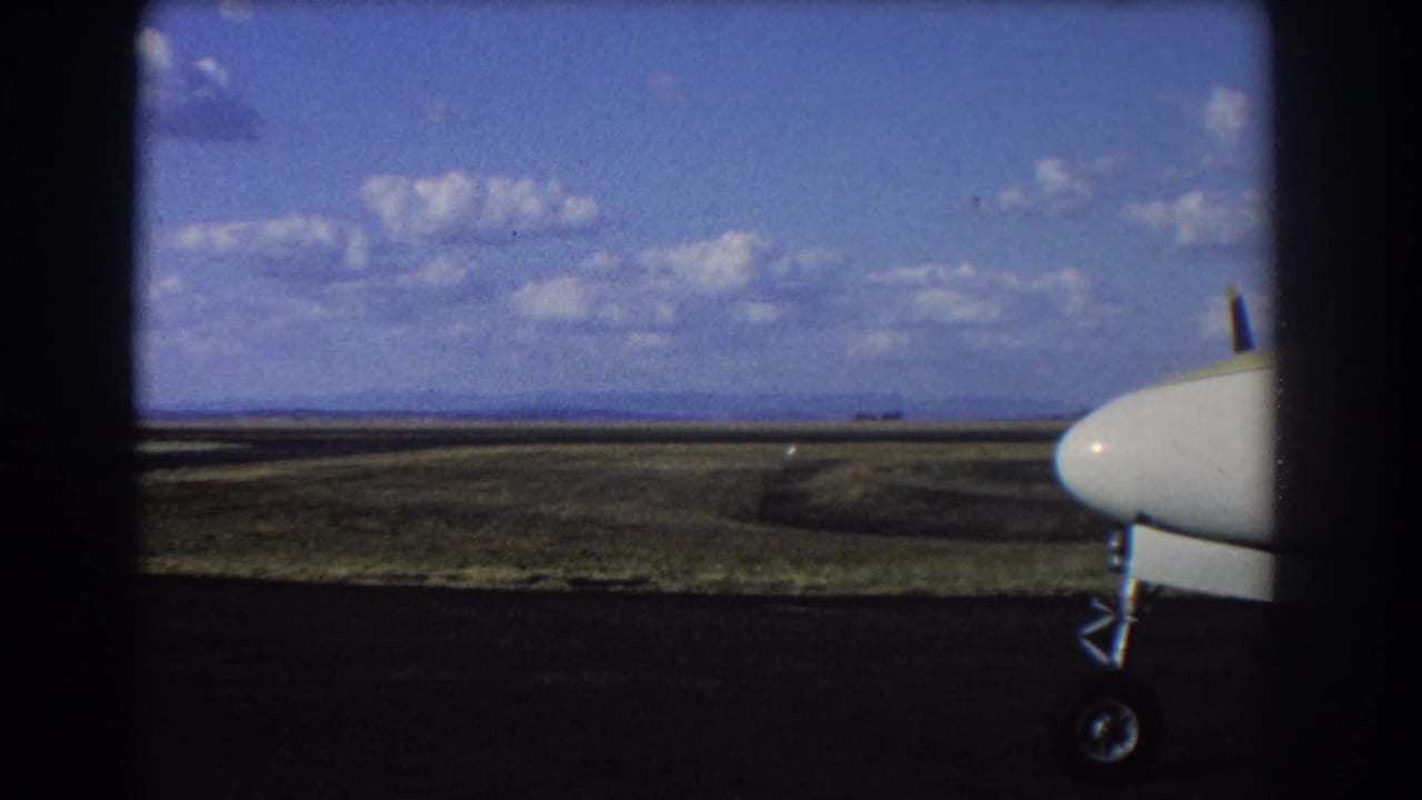 Aircraft nose at the right edge with runway and distant landscape under scattered clouds.