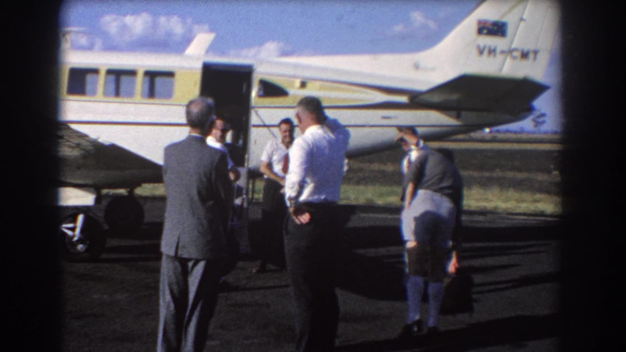 In Brisbane, Australia in 1967, men in suits and shirts stand near the open door of a small white and yellow aircraft on the tarmac.