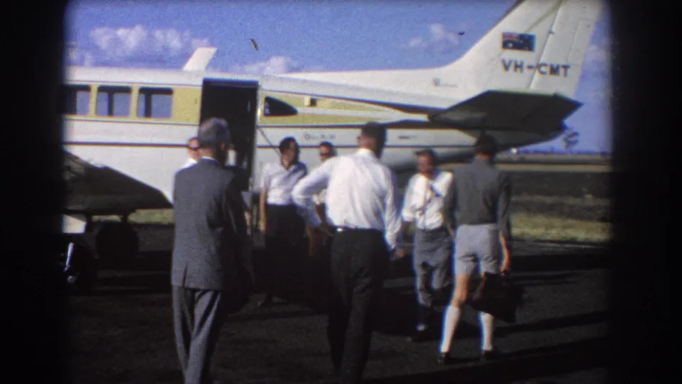 Men in 1960s attire walk and stand around the open door of a small aircraft marked VH-CMT in Brisbane, Australia.