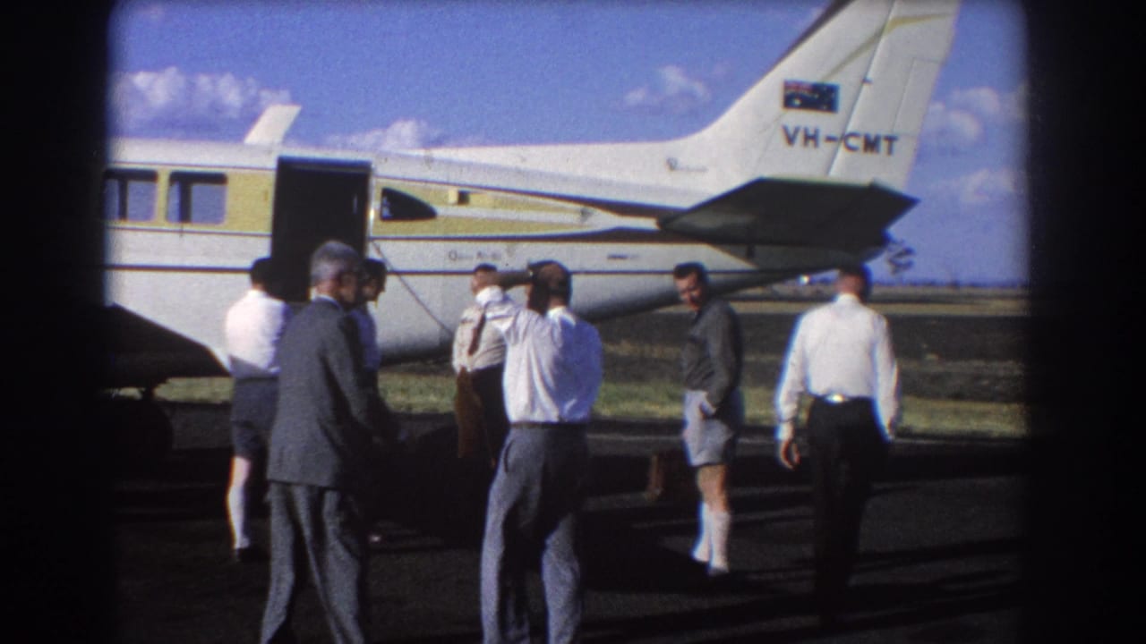 Men stand beside an open white-and-yellow aircraft on an airfield.