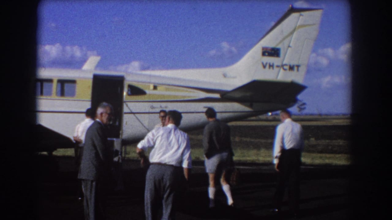 Men stand and walk near the open door of a small aircraft.