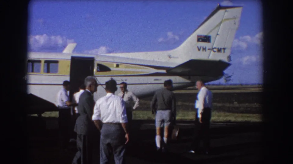 The 1967 Brisbane footage shows men in suits, shirts, and shorts gathered beside the open aircraft door.