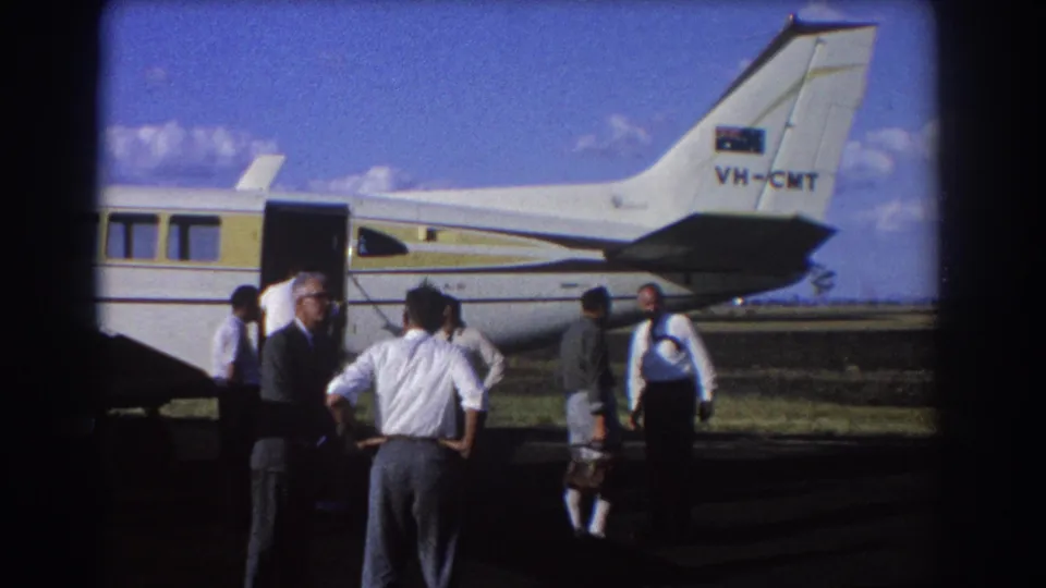 At the Brisbane airfield in 1967, men stand near the open door of a white-and-yellow aircraft marked VH-CMT.