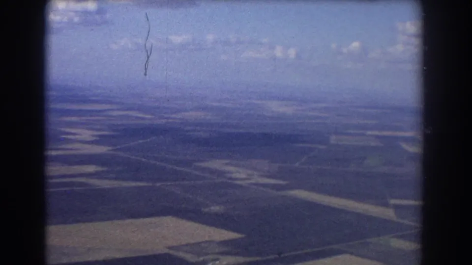 Passenger-view aerial footage near Brisbane in 1967, with fields, roads, clouds, and visible 8mm frame edges.