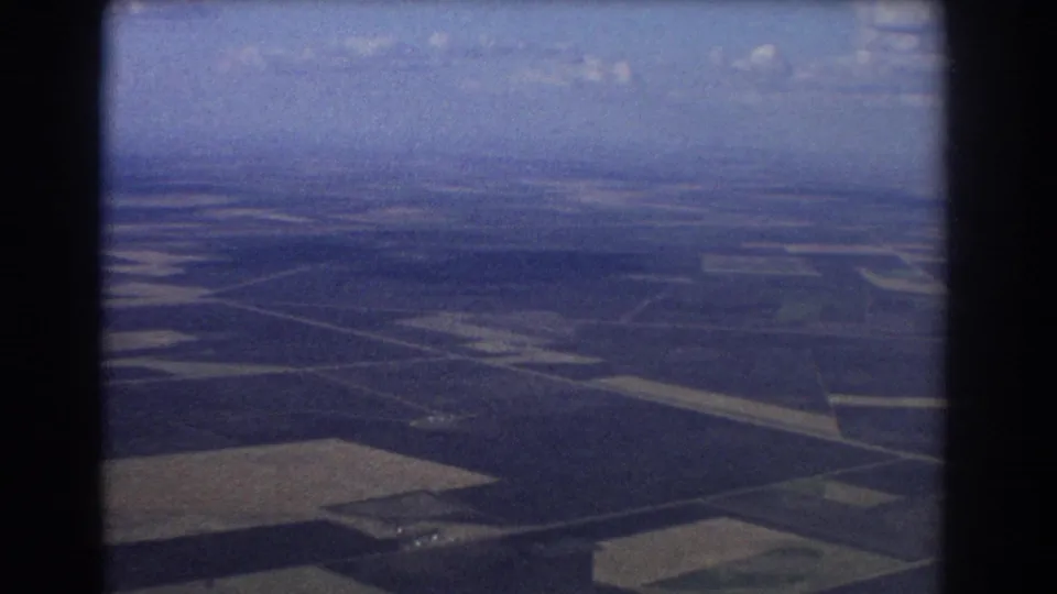 8mm home-movie aerial view from the Brisbane travel clip, showing divided farmland and a hazy horizon.