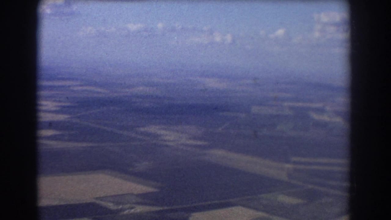 1967 Brisbane-area 8mm aerial view showing open fields and distant hazy terrain through soft aircraft-window framing.