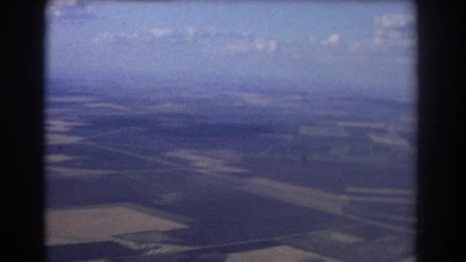 1967 Brisbane-area 8mm aerial view showing open fields and distant hazy terrain through soft aircraft-window framing.