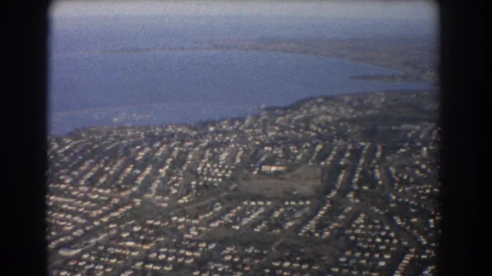 1967 Brisbane-area aerial view of suburban blocks, road networks, open land, and a shoreline or broad waterway.