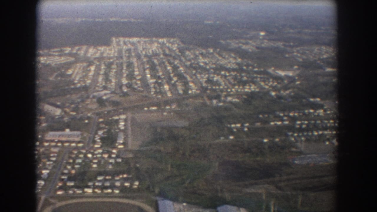 Aerial view of a suburban neighborhood with roads and open fields below.