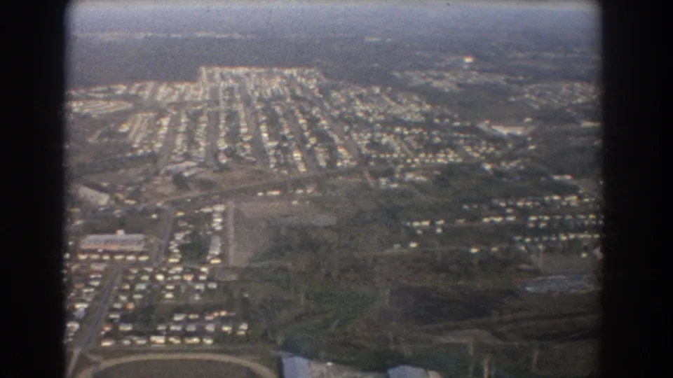 Brisbane-area aerial view from 1967 showing rows of houses, road patterns, and open ground beyond the aircraft window.