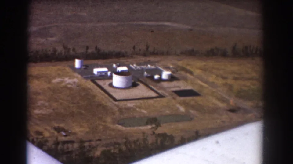 Brisbane-area 8mm aerial frame showing storage tanks, access roads, open paddocks, and a white airplane wing edge.
