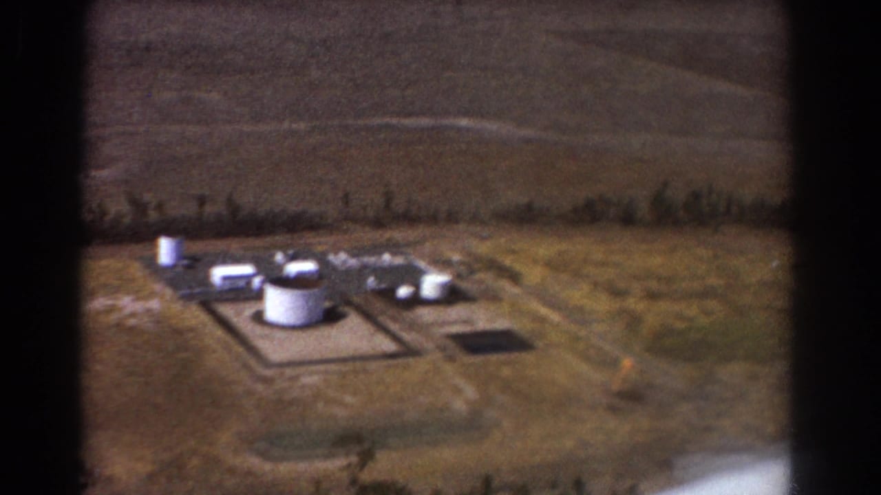Aerial view of white storage tanks and buildings in open dry terrain.