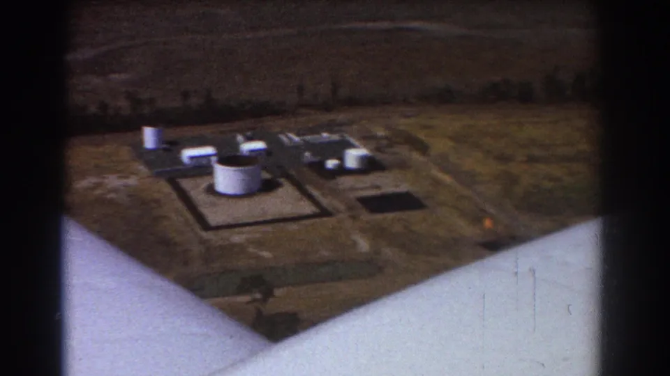 Aerial frame from the 1967 Brisbane footage showing white tanks, small structures, roads and part of the aircraft edge.