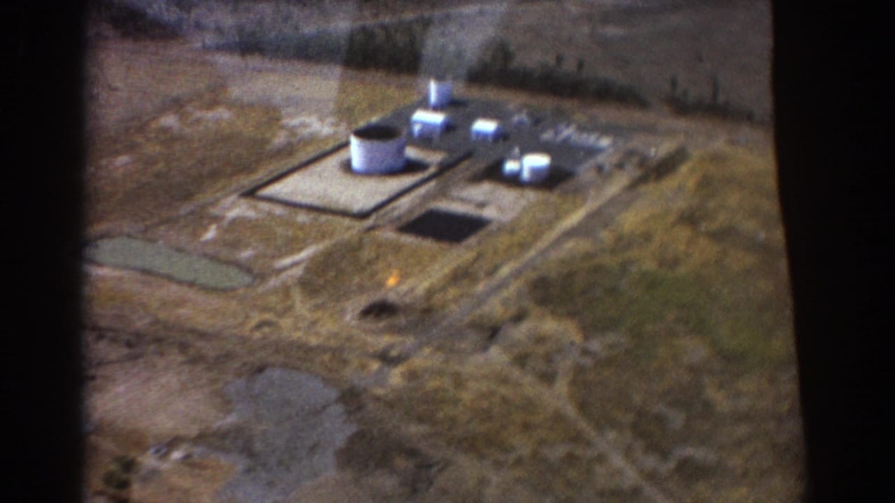 Aerial view of an industrial facility with white tanks, low buildings, dry ground, and aircraft-window framing.