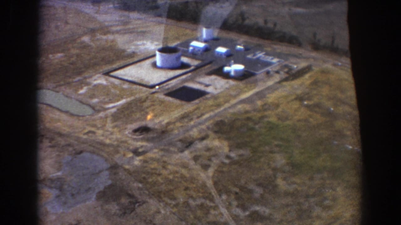 Aerial view of tanks and low buildings at an isolated industrial site, with dark window edges visible.