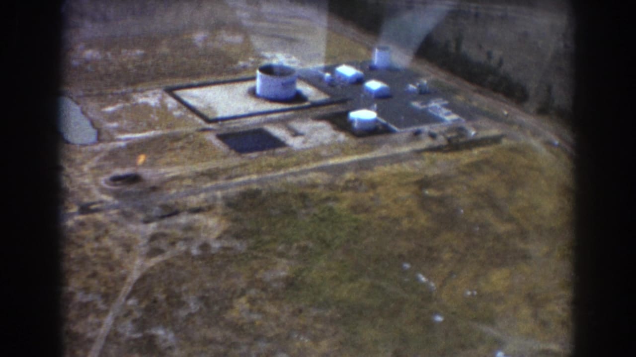 Aerial view of an industrial complex with tanks, buildings, fields, and dark window-frame edges.