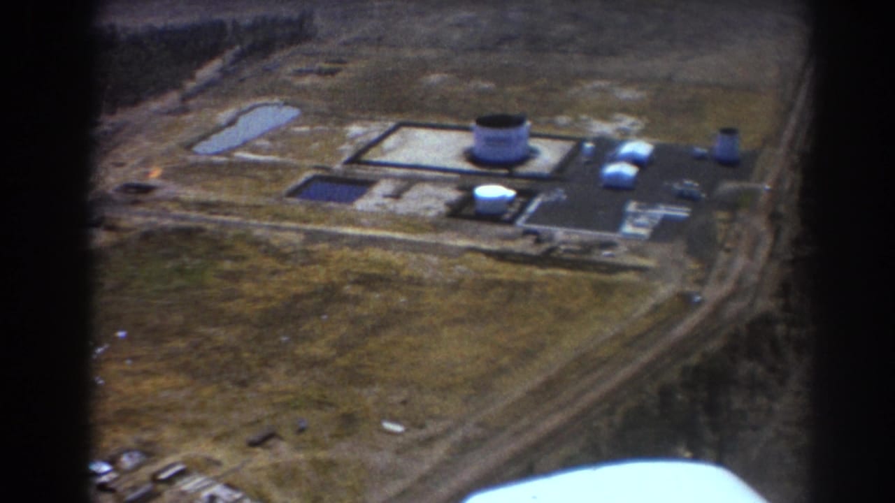 Aerial view of an industrial complex with tanks, buildings, roads, ponds, and open land.