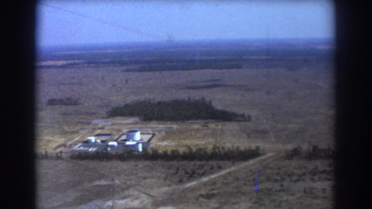 Aerial view of flat plains with a small industrial complex and white tanks below.
