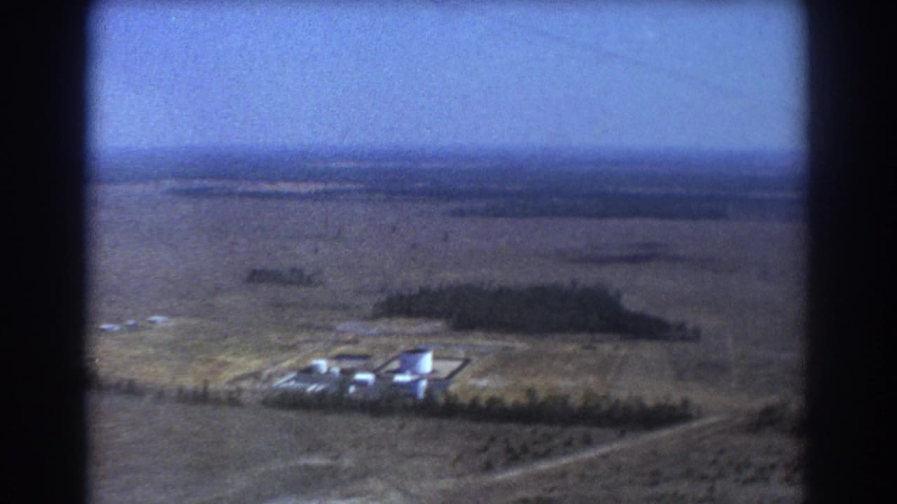Industrial tanks and low buildings seen from above across open rural land.