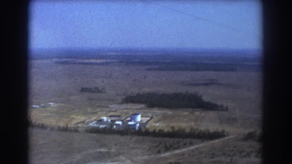 Aerial 8mm frame from Brisbane, Australia, showing an industrial complex amid dry plains with trees and distant terrain.