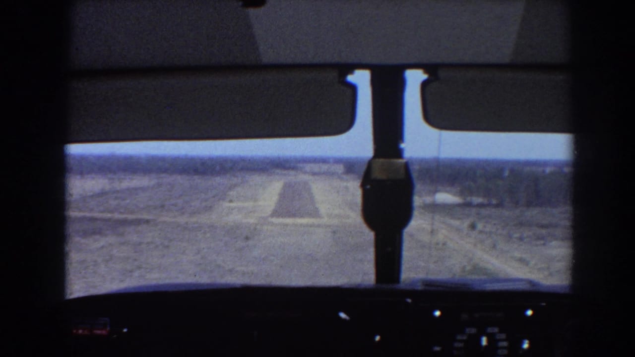 Cockpit windshield view toward a narrow runway over flat terrain.