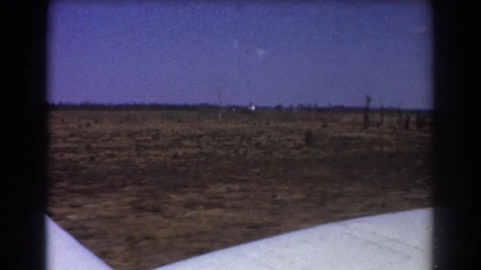 Aircraft wing seen from a passenger window over arid ground during a 1967 Australian travel sequence.