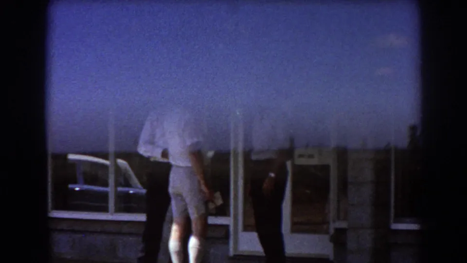 Men in light shirts stand near a glass doorway, partly obscured by glare and film framing.