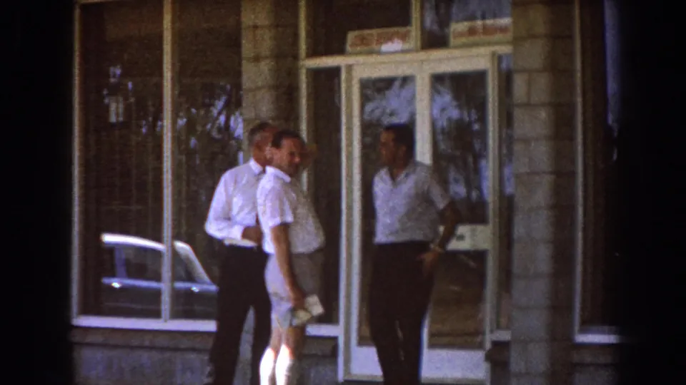 Three men stand outside a building entrance in Brisbane, Australia, during a 1967 business travel home movie.