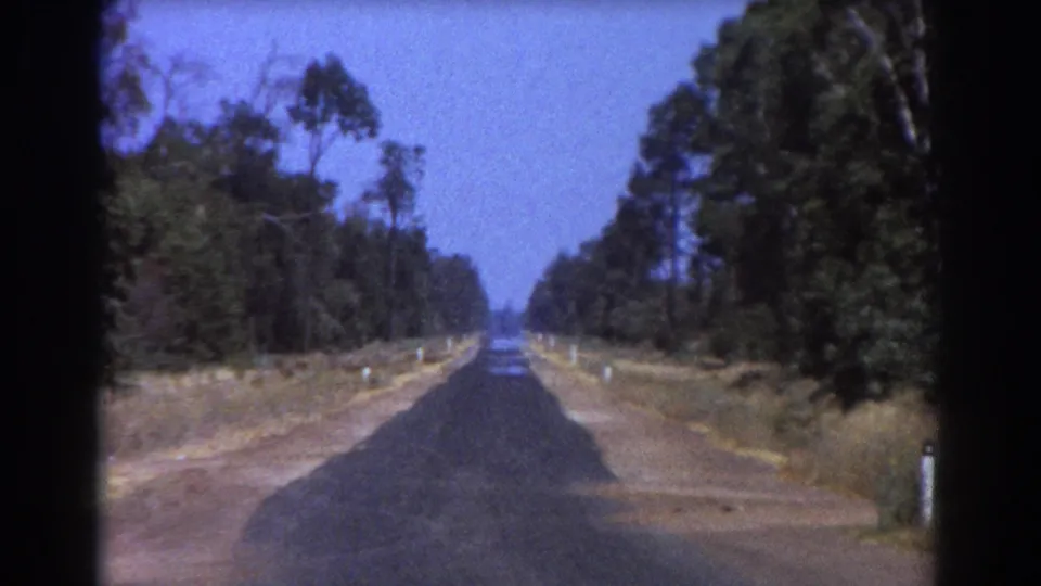 1967 Brisbane-area travel frame with a straight country road, wooded verges, dry shoulders, and visible 8mm frame borders.