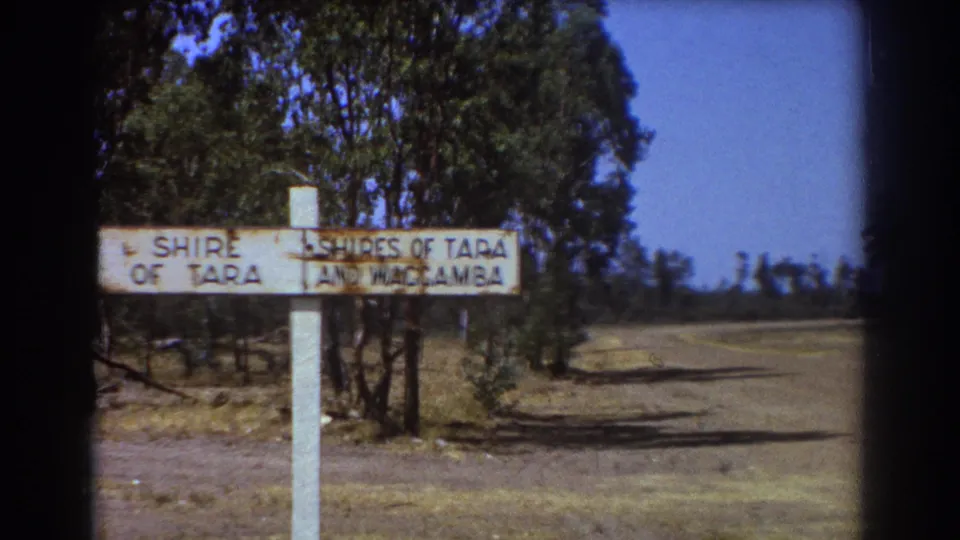 A slightly shifted 8mm view of the Shire of Tara and Waggamba sign shows the post, dry verge, trees, and road under clear sky.