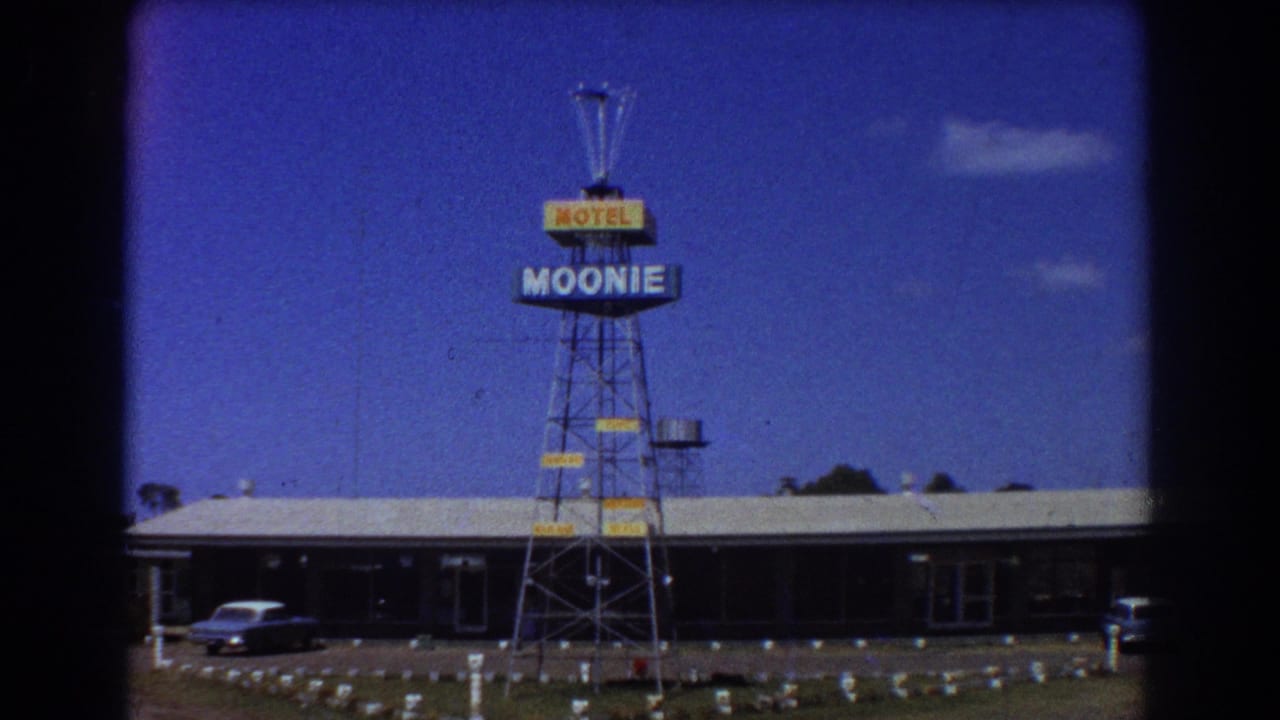 Roadside motel with a tall Moonie Motel sign and a parked car under blue sky.