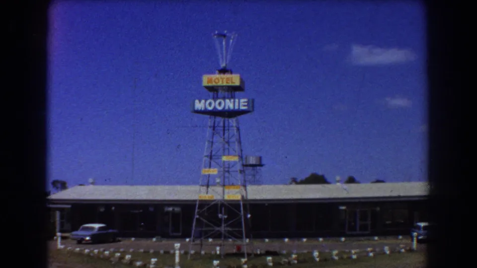 1967 Brisbane footage showing a low roadside motel, a tall Moonie Motel sign, lawn area, and parked car under a bright sky.