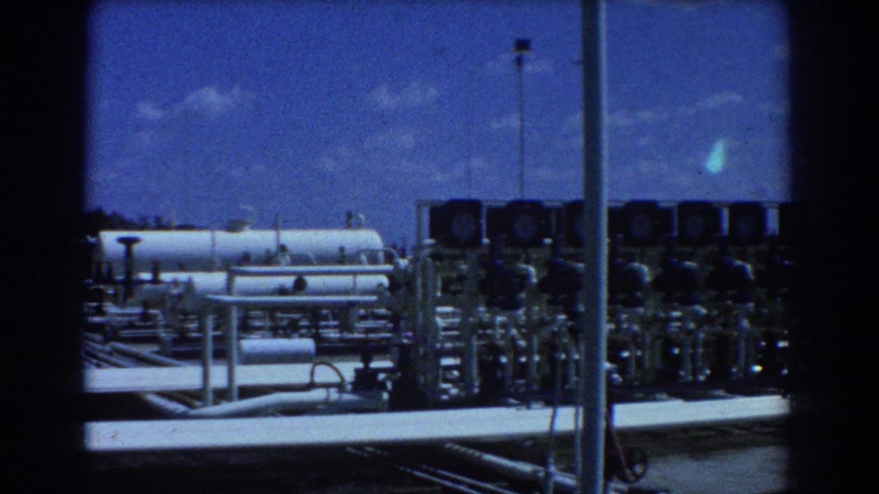 Industrial oil yard with white tanks, pipes, valves, and lighting poles.