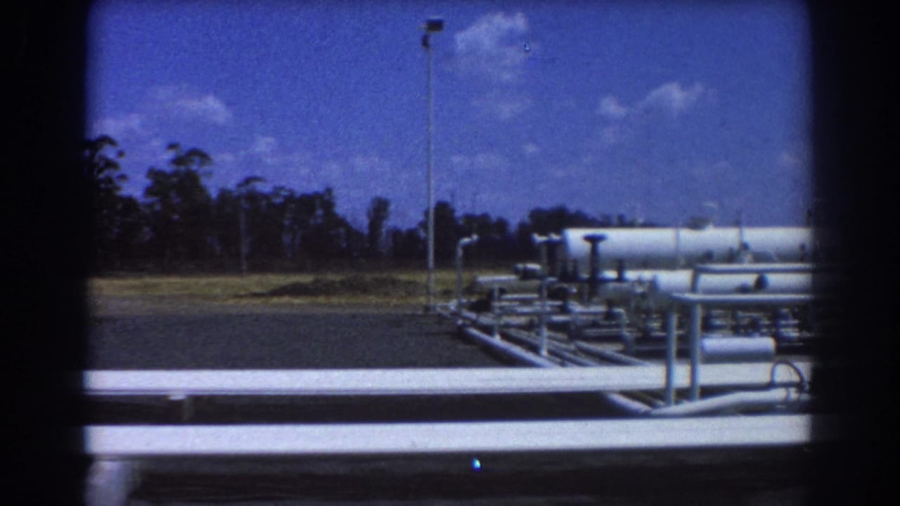 White industrial pipes and tanks beside an asphalt lot under a blue sky.