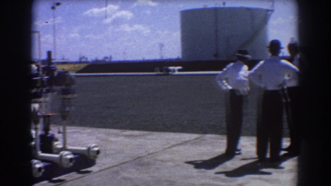 Three men in white shirts and dark trousers stand talking at a Brisbane industrial site in 1967, with a large tank behind them.