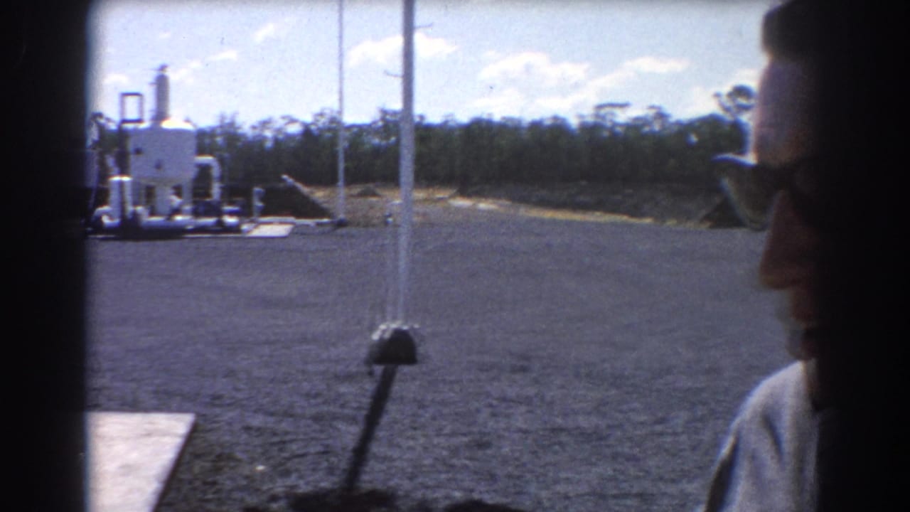 Gravel industrial yard with white oil equipment and a man partly visible at right.