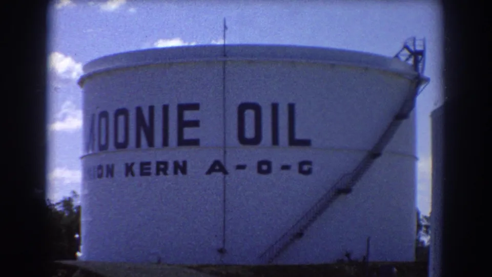 1967 Brisbane frame focused on a large white cylindrical tank marked MOONIE OIL and UNION KERN A-O-C under a bright blue sky.
