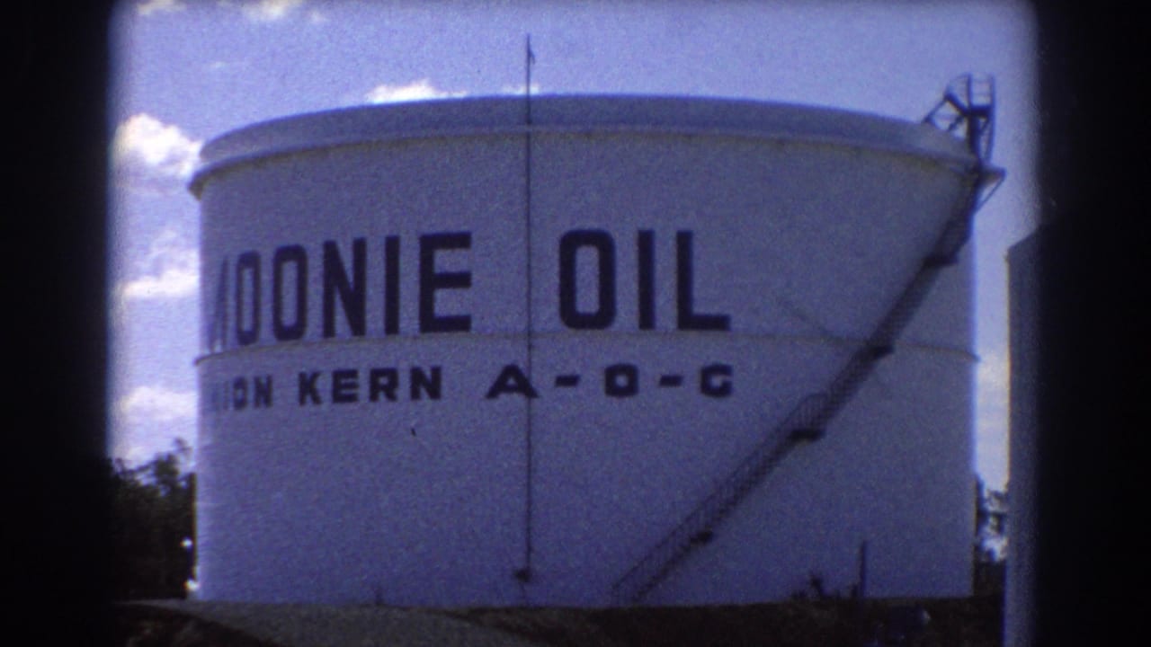 Large white Moonie Oil storage tank with painted lettering, ladder, and blue sky.