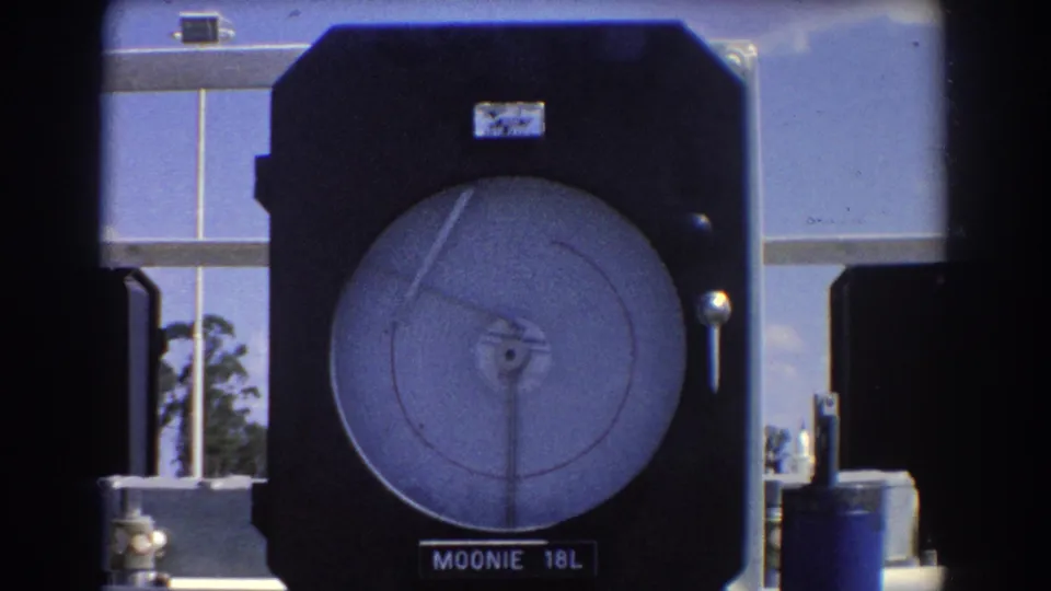 Final 8mm frame of the Moonie 18L industrial gauge, with its circular dial and needle framed against metal equipment and sky.