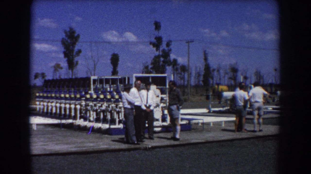 Several men stand beside blue-and-white water treatment valves at an outdoor facility.