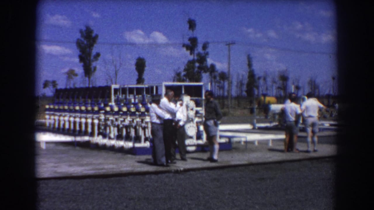 Several men at a Brisbane water treatment site appear to discuss the valve equipment beside a paved pad and sparse trees.