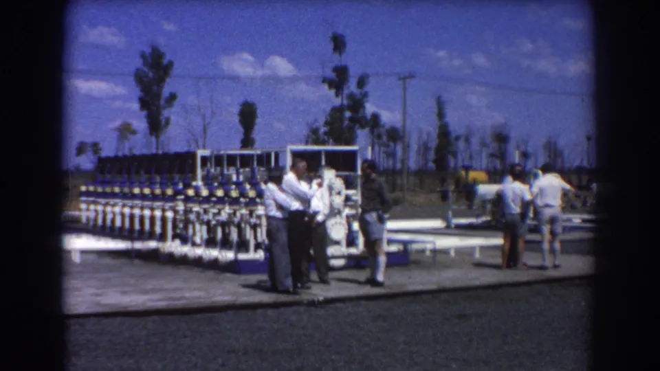 Several men at a Brisbane water treatment site appear to discuss the valve equipment beside a paved pad and sparse trees.