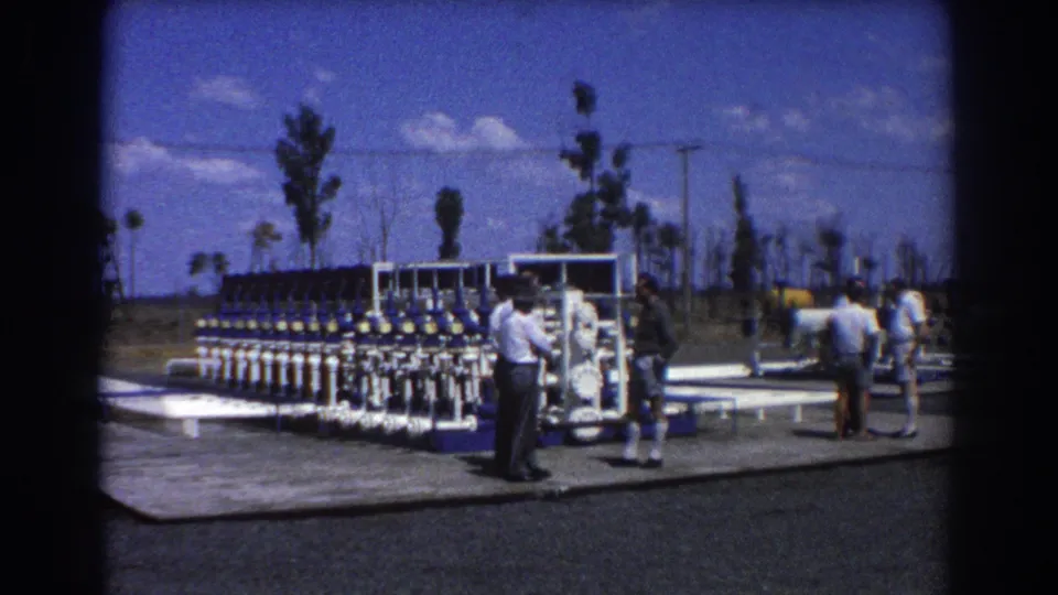 Late in the clip, the Brisbane water treatment site remains framed with valve rows, white pipework, men, trees, and open sky.