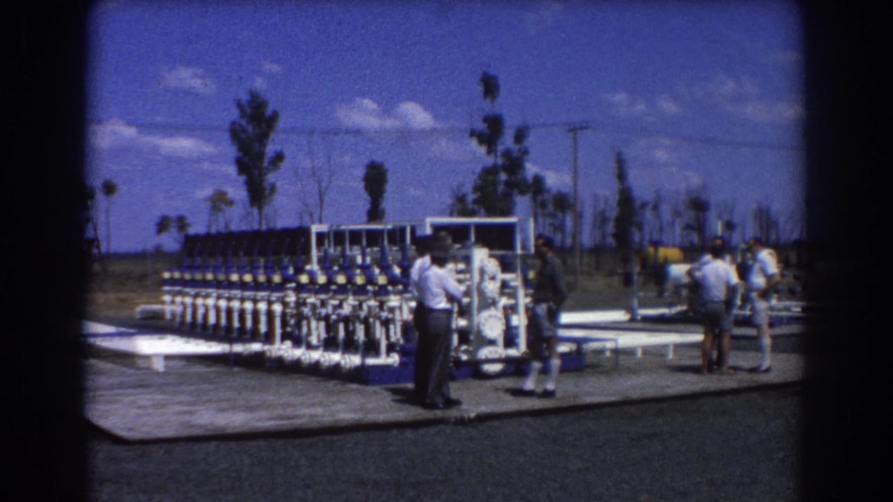 Men standing beside blue and white industrial pipe equipment outdoors.