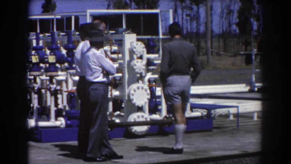 Closer 8mm view of two men near valve wheels and blue pipe equipment during an outdoor industrial inspection in Brisbane.