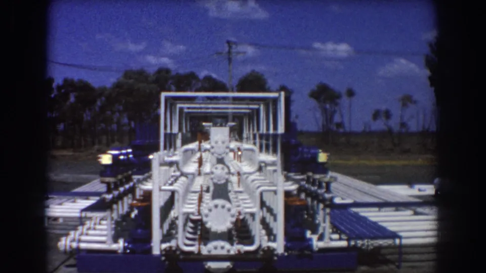 Head-on view of white industrial pipework and blue pump machinery in Brisbane, shown with trees and open sky behind it.