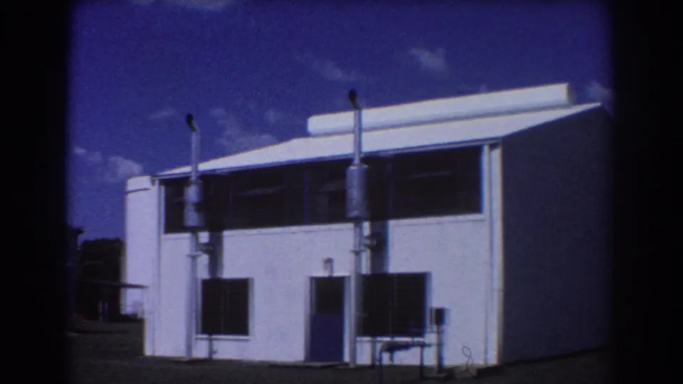 1967 Brisbane frame of a sunlit white building with louvered windows, a blue door, metal exterior fixtures, and open yard space.