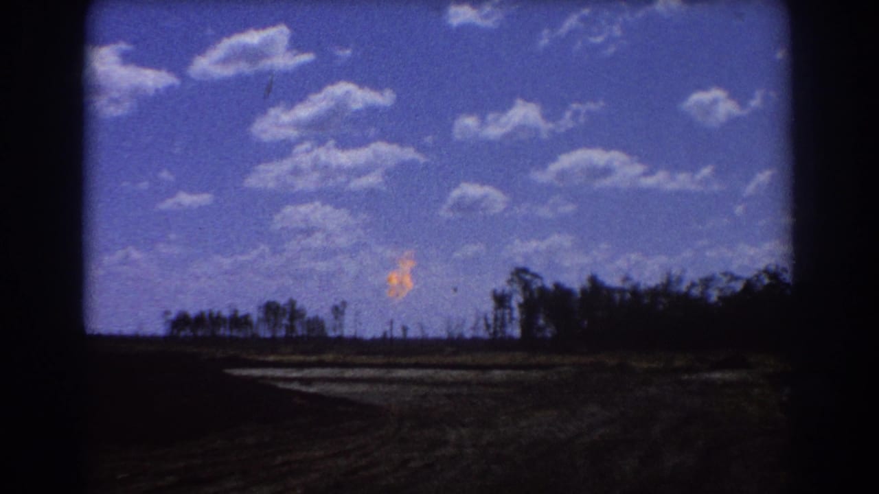 Distant orange flare above a dark treeline under a blue sky with scattered clouds.