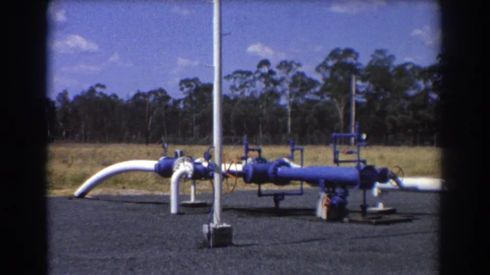 1967 Brisbane 8mm view of blue and white industrial pipes and valves in an open field setting.