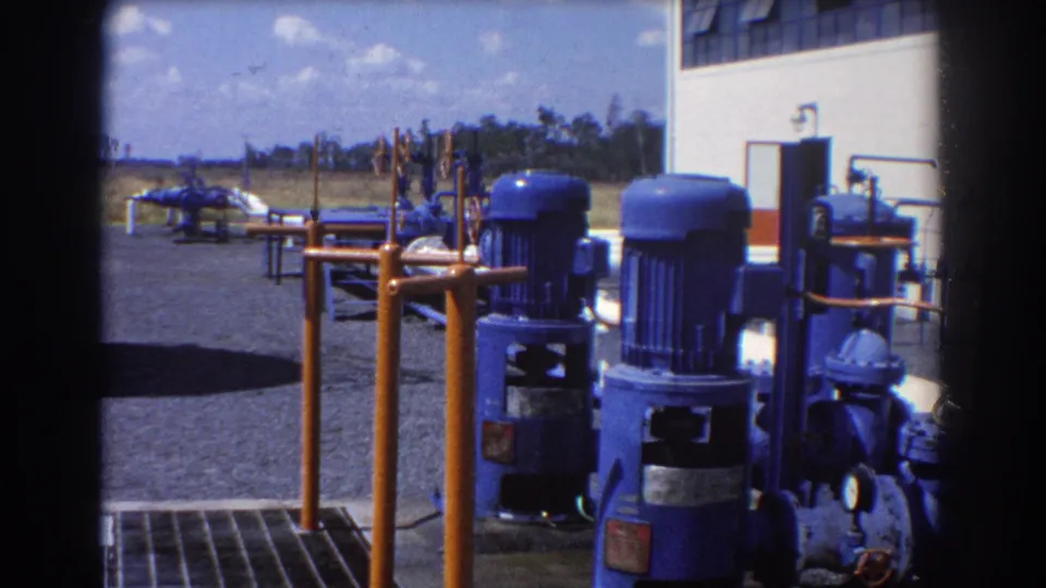 1967 Brisbane 8mm view of blue pump equipment, orange railings, metal grate flooring, piping, and an open industrial yard.